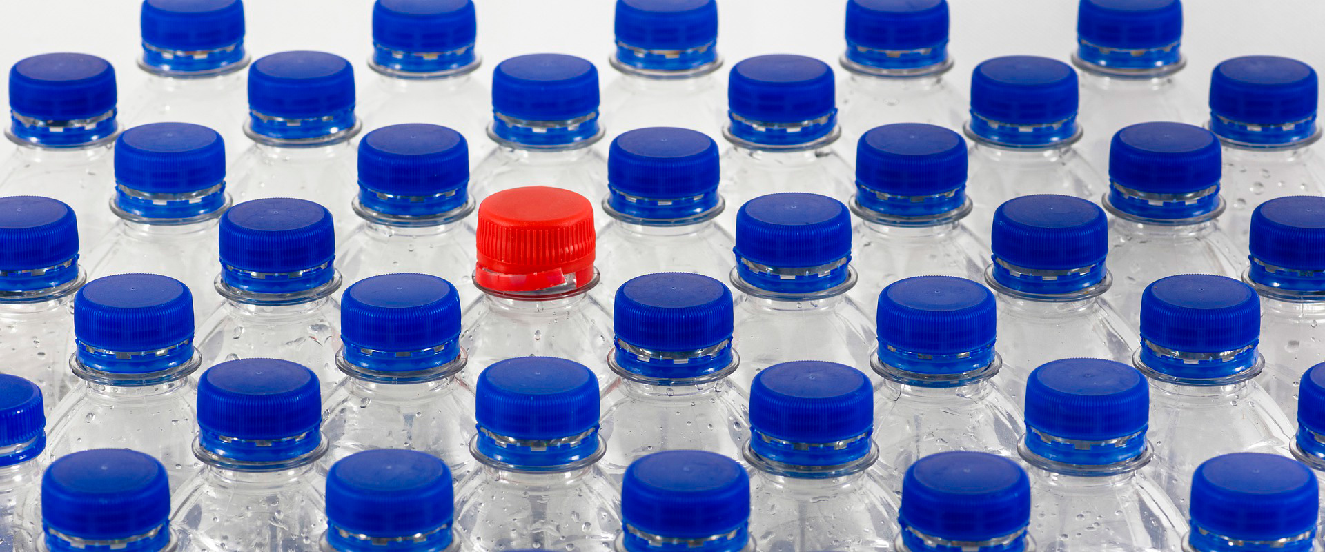 Bouteilles PET avec bouchon rouge entre plusieurs bouteilles avec bouchons bleus